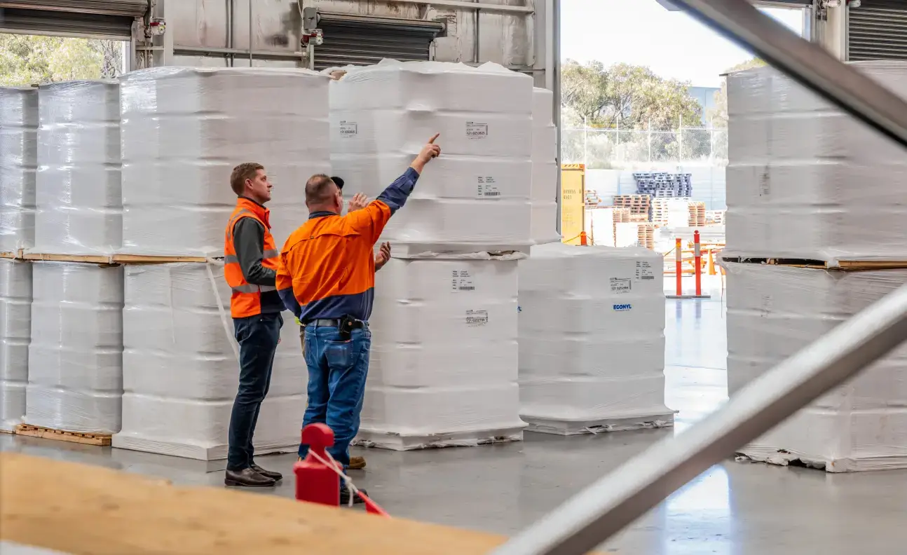 Warehouse staff reviewing palletised stock inside warehouse facility.
