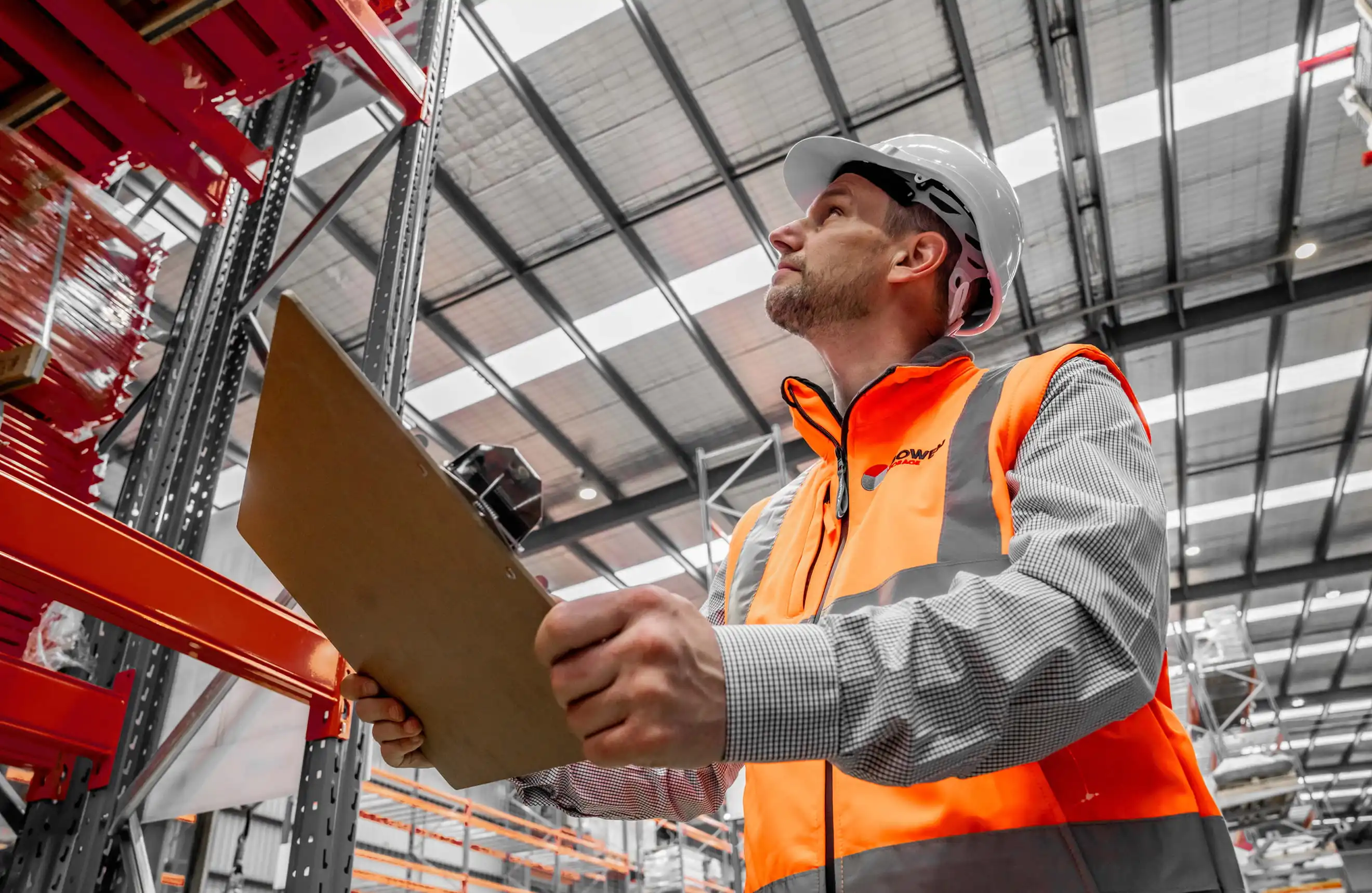 Warehouse supervisor inspecting pallet racking and recording findings on an inspection checklist.